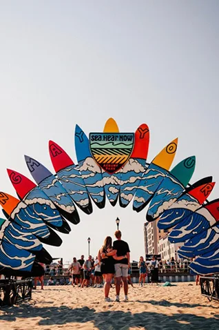Couple at Asbury Park Beach NJ posing under the "Sea.Hear.Now." Festival surfboard archway