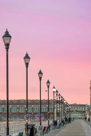 Asbury Park Boardwalk with a row of streetlights at sunset and buildings in the background
